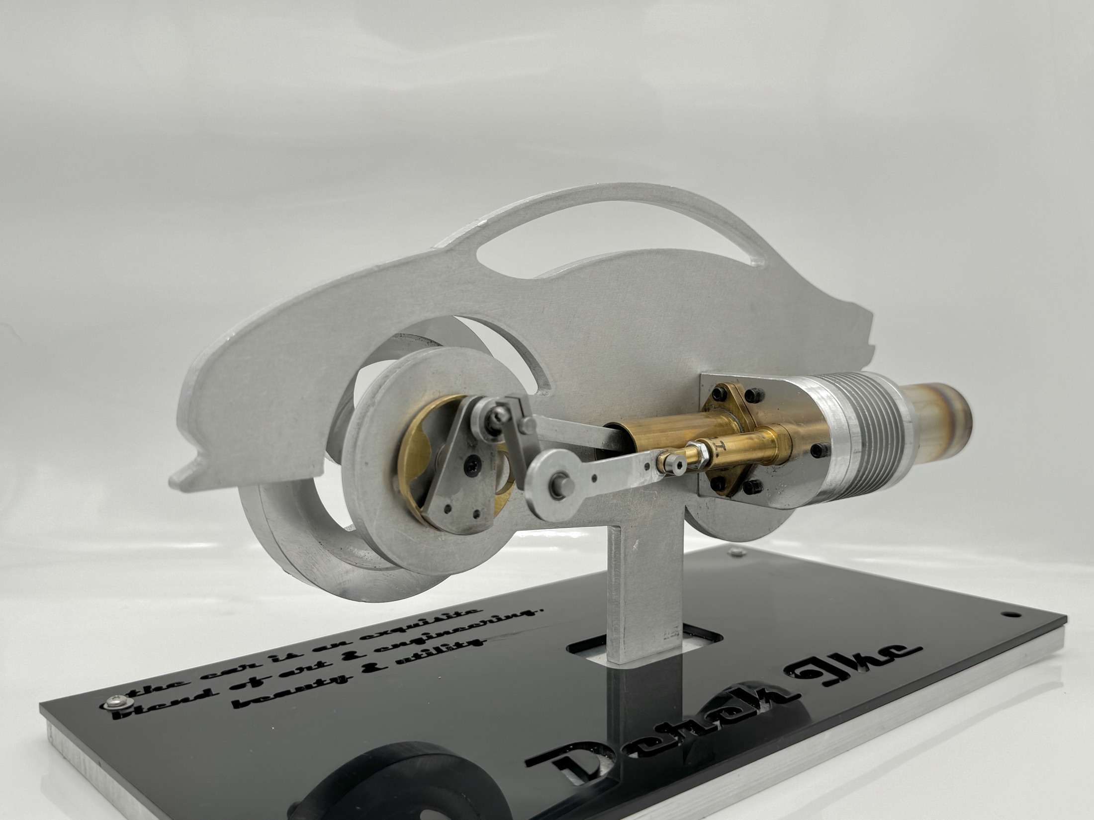 The finished Stirling engine on its laser-cut aluminum sports-car silhouette bedplate, mounted over the black acrylic base with the owner's name engraved into it
